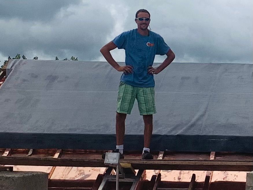 A man in a blue shirt and green shorts is standing on a roof with his hands on his hips.