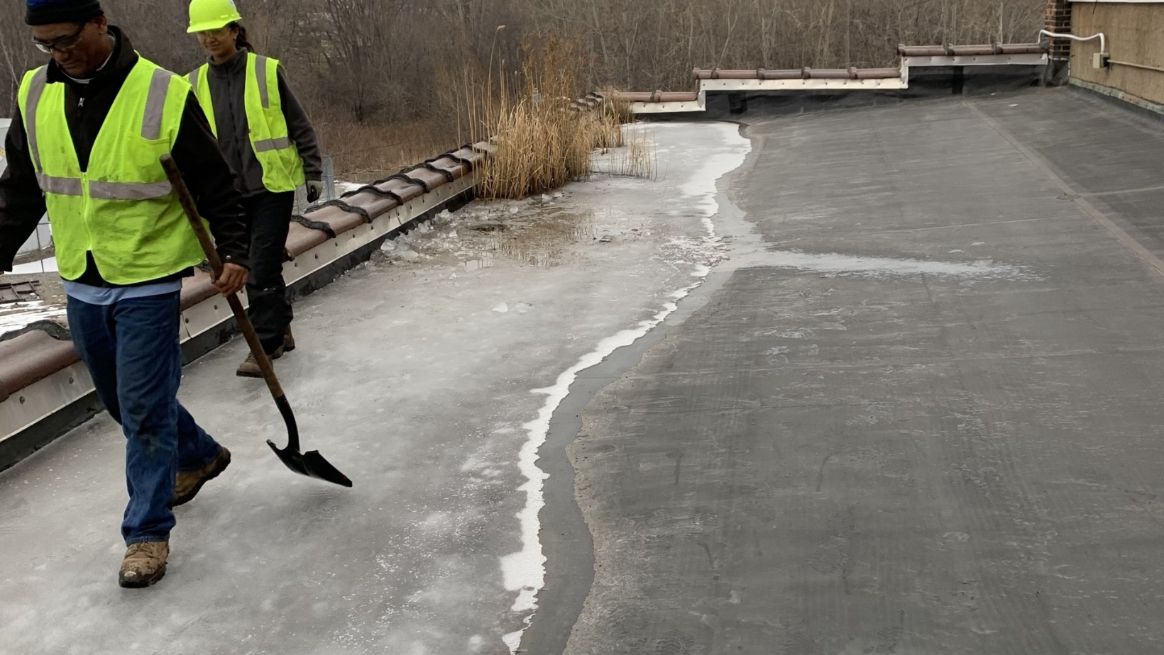 Roofers in neon safety vests on a flat roof with ice dams in Vermont