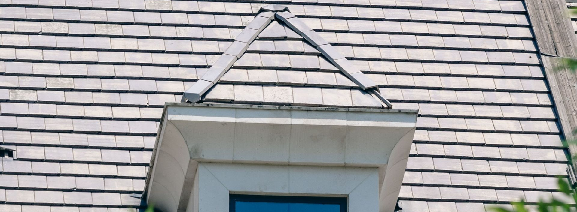 Gray shingle roof with a small dormer window and triangular trim above a blue-framed opening