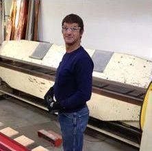A man is standing in front of a boat in a garage.