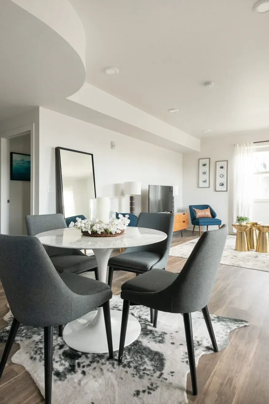 Modern dining area with a round marble table and four gray chairs.