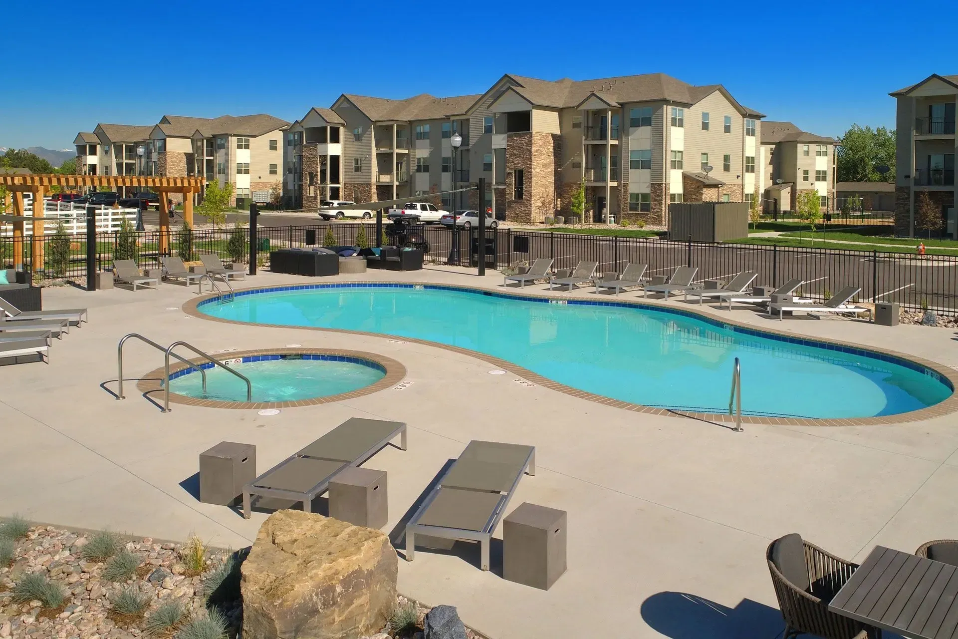 Outdoor swimming pool and hot tub with lounge chairs and seating areas at an apartment complex.