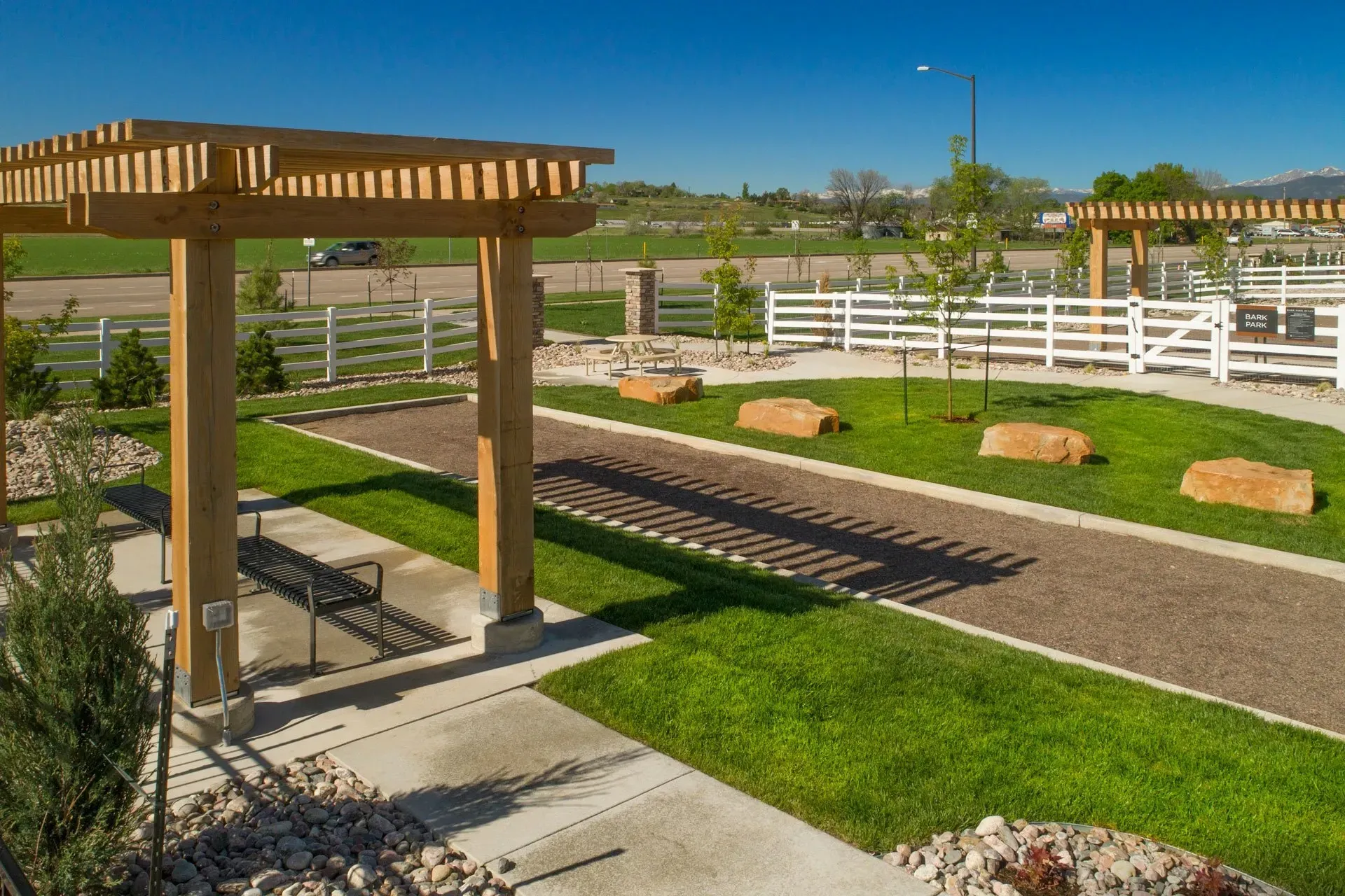 Outdoor dog park with a white fence, benches, and a pergola.
