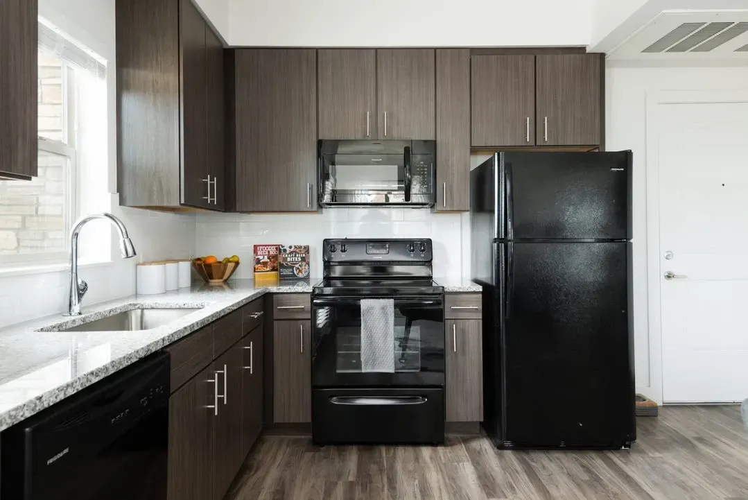 Modern kitchen with dark wood cabinets, granite countertops, stainless steel sink, black appliances, and a white door.