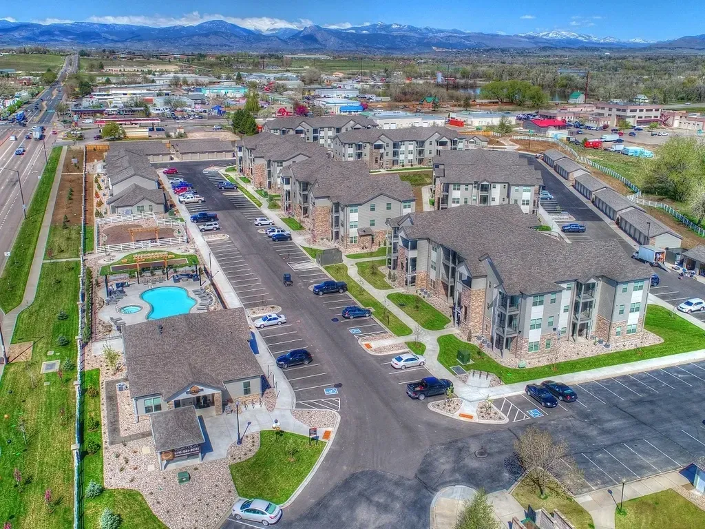 Aerial view of a multifamily property with apartments, a pool, and surrounding landscape.