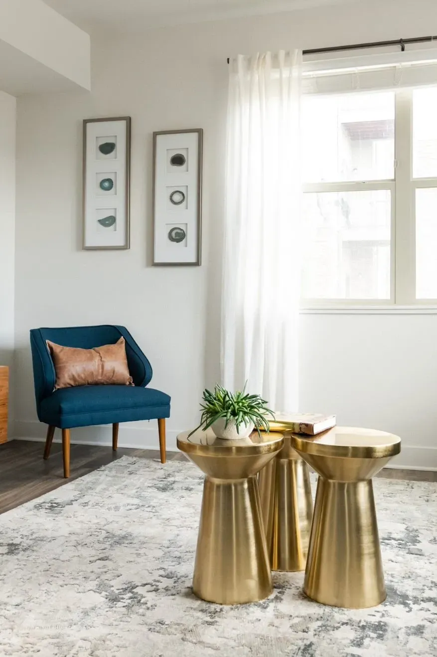 Stylish living room with a blue accent chair, gold side tables, and abstract art.