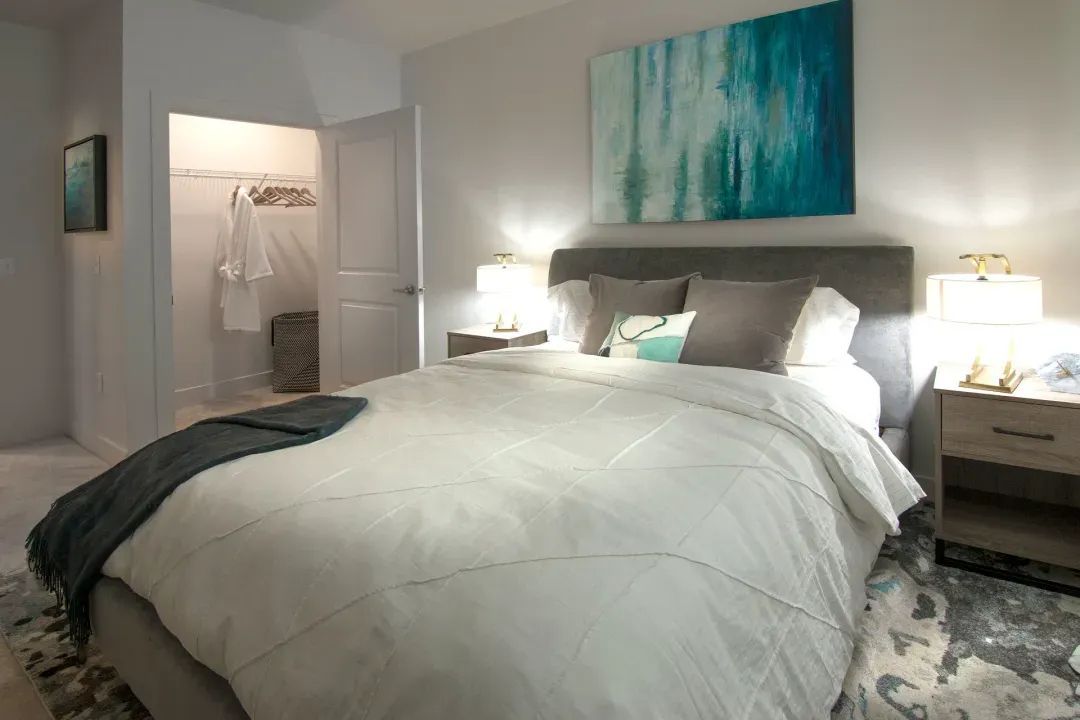 Modern bedroom with a white bed, teal wall art, and a dresser with lamps