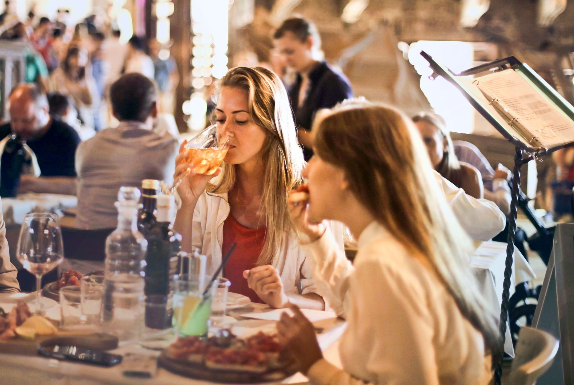 People dining at an outdoor restaurant, with wine glasses, plates, and a menu on the table.