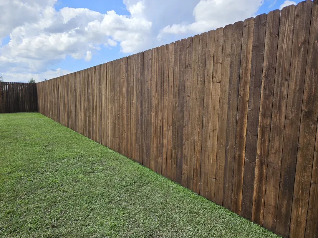 Long wooden fence bordering a grassy yard under a partly cloudy sky