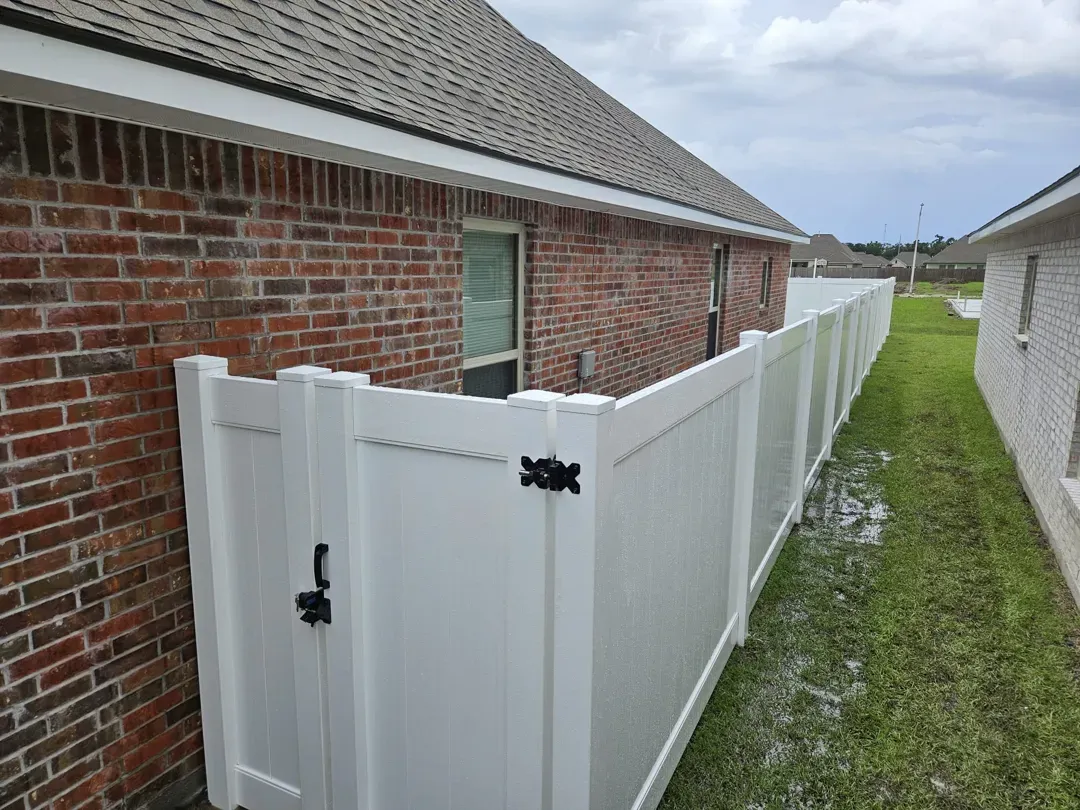 White vinyl fence along a brick house beside a narrow grassy path