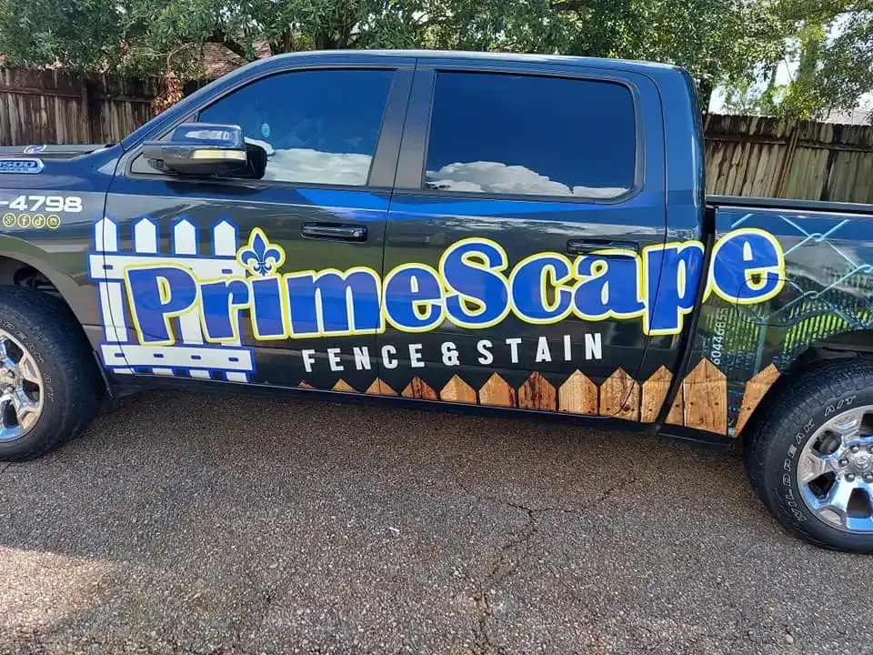 Blue pickup truck with large PrimeScape Fence & Stain logo parked on gravel road