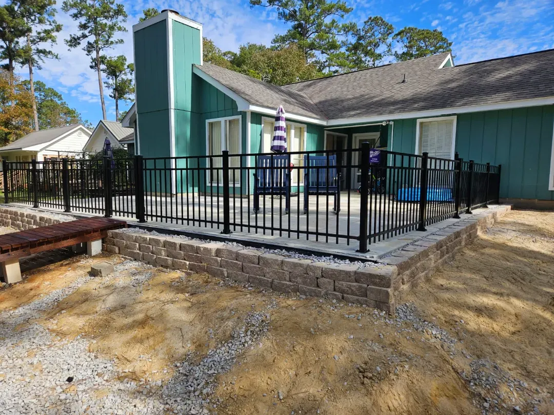 Accessible patio with black railing beside a teal house and raised deck.