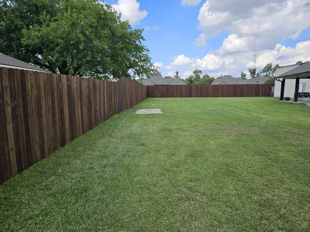 Wide grassy backyard with a wooden fence, trees, and a partly cloudy sky