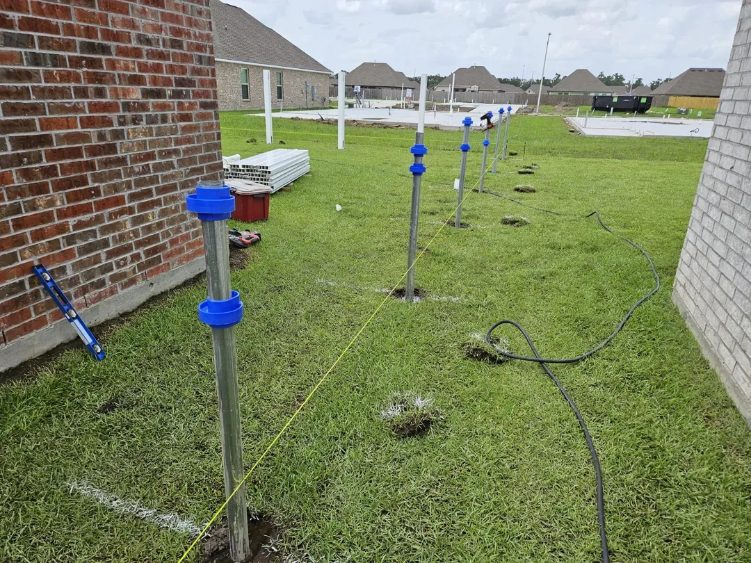 Gas and utility piping with blue caps along a grassy side yard beside brick houses