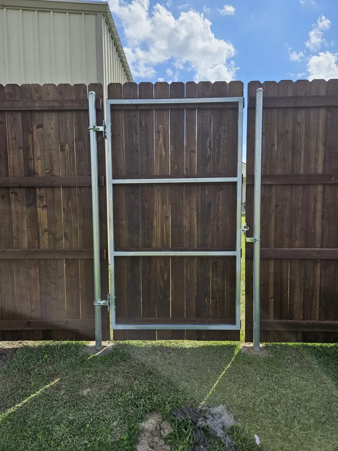 Wooden fence with a narrow gate frame beside a house and grassy yard