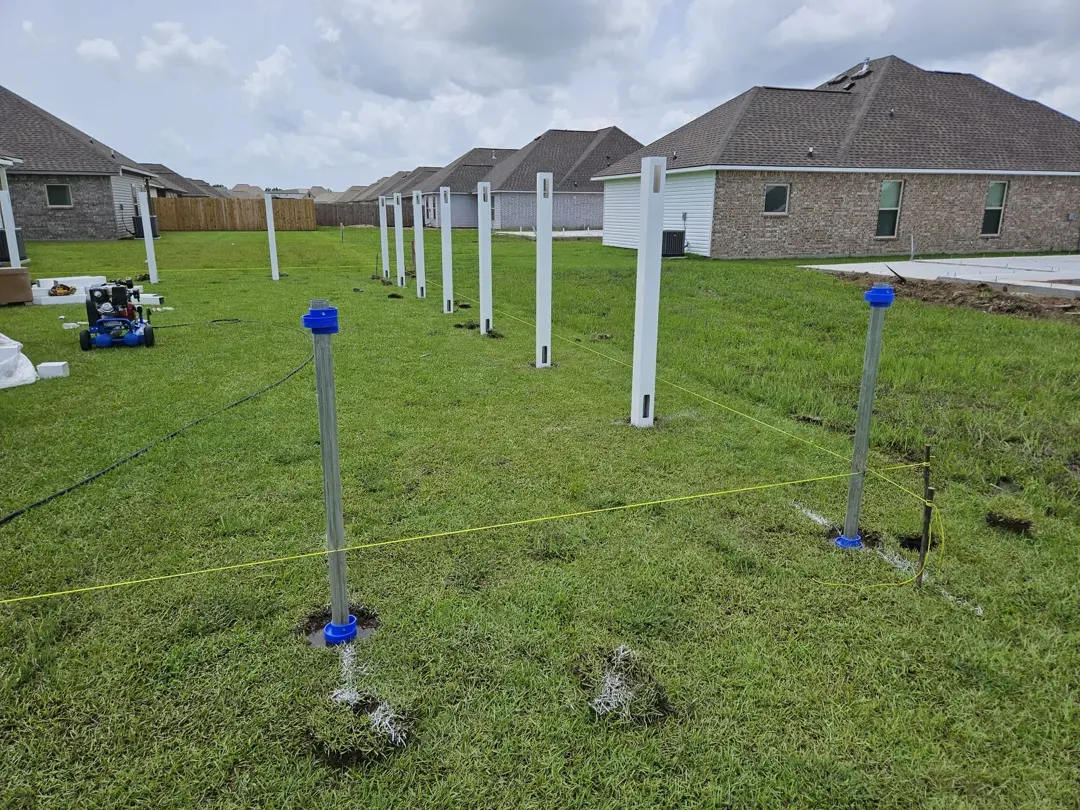 Backyard with white survey stakes and blue markers on green grass near houses