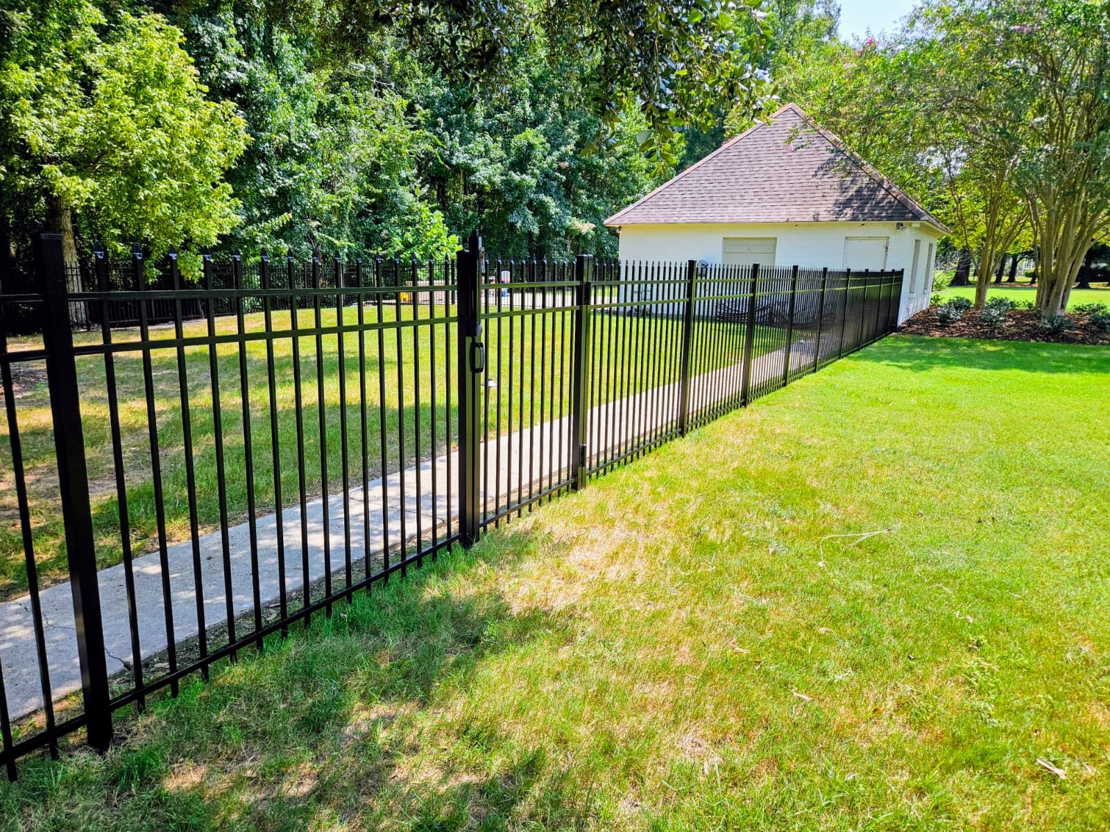 Black metal fence beside a grassy path leading to a small white gazebo in a park