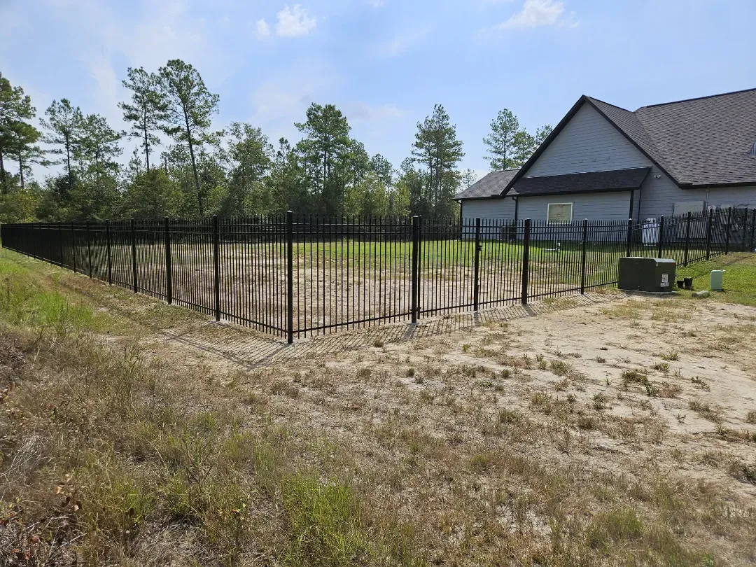 Backyard with young trees protected by black fencing beside a house under a clear sky