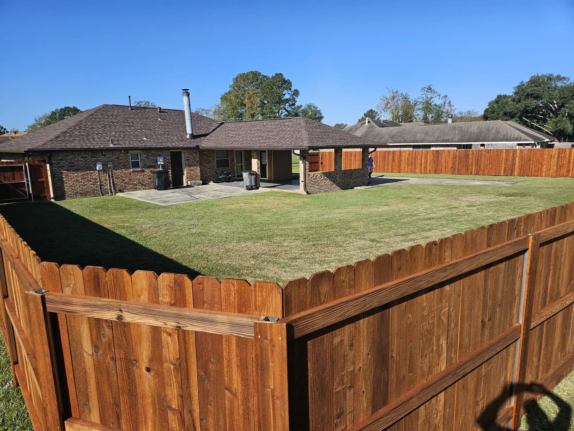 Wooden privacy fence enclosing a grassy backyard behind a single-story house on a sunny day
