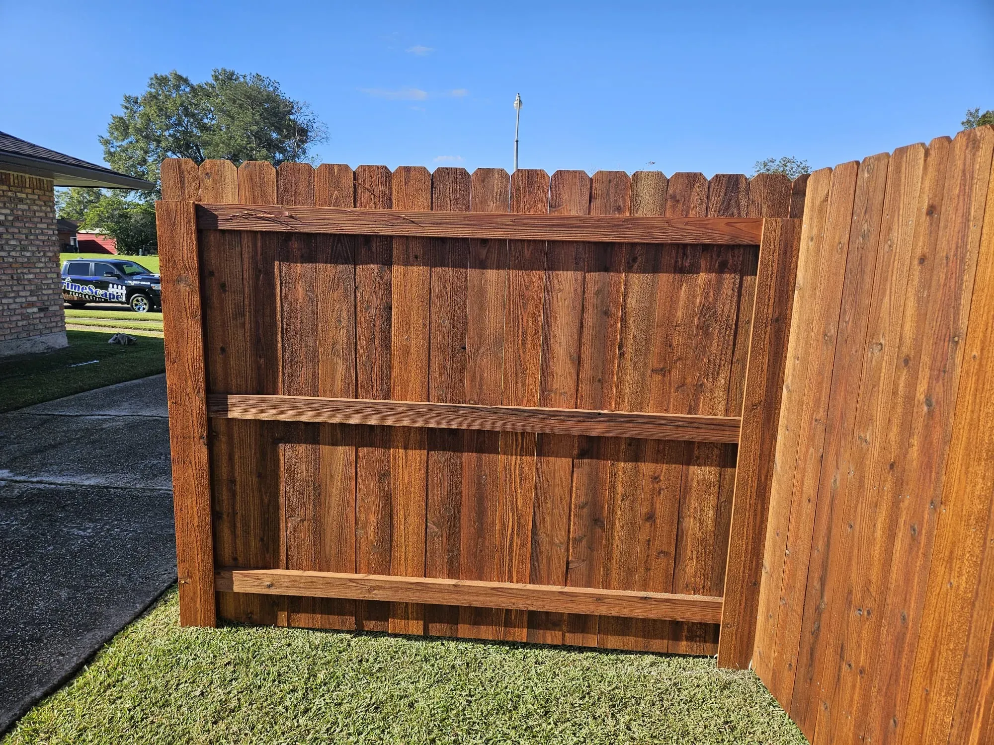 Wooden backyard fence and gate with horizontal support rails under a blue sky