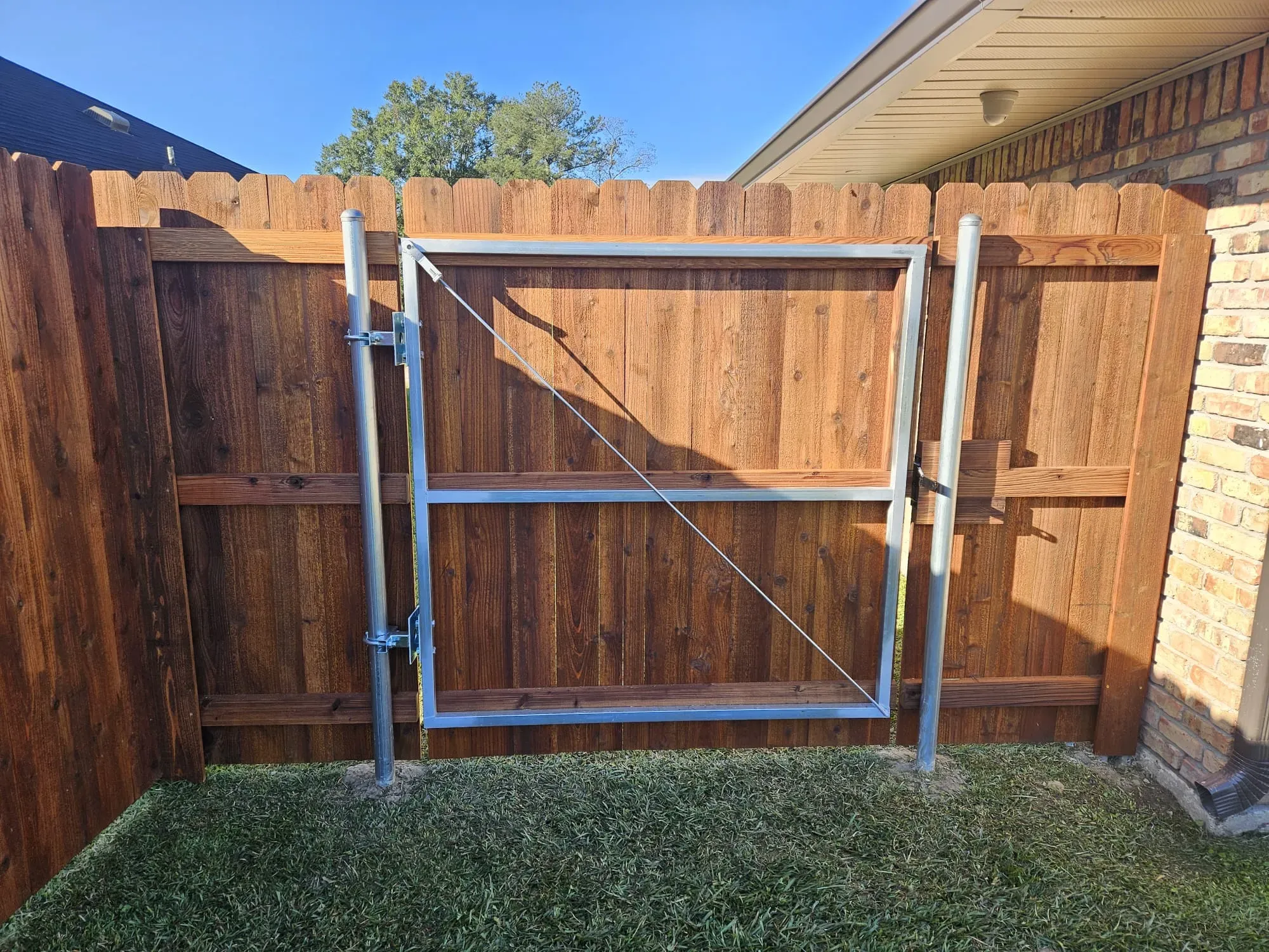 Metal gate in a wooden backyard fence beside a grassy lawn, in bright sunlight