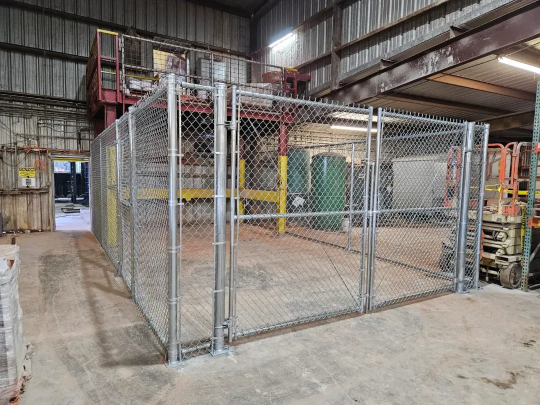 Chain-link fenced industrial enclosure inside a warehouse, with a concrete floor and metal equipment nearby.