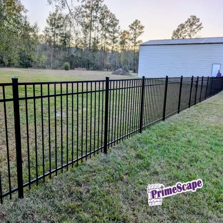 Black metal fence along a grassy yard beside a white building at dusk