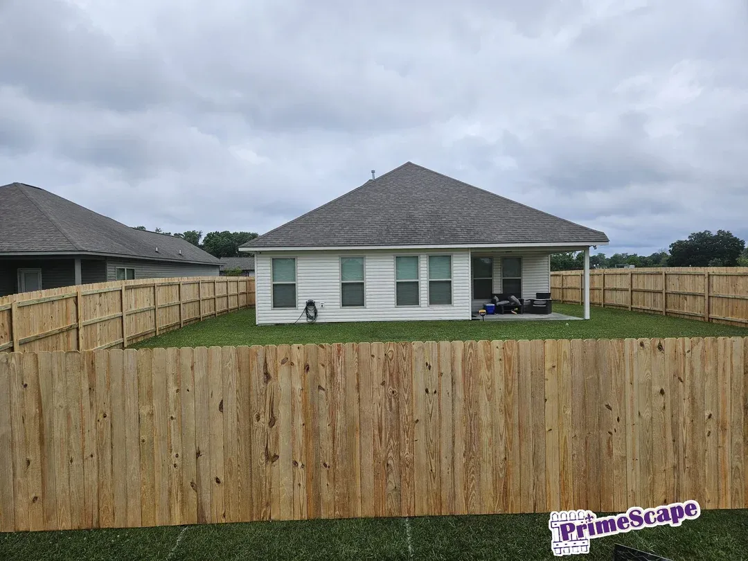 Backyard with a white house, tall wooden fence, and cloudy sky