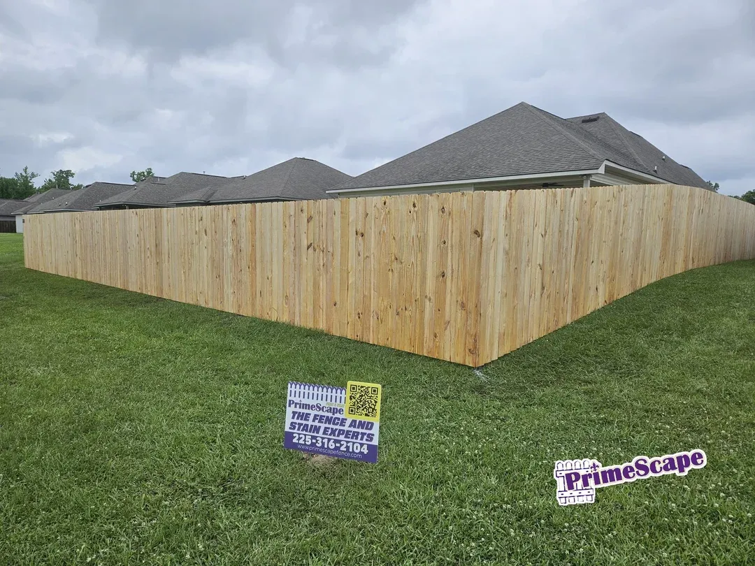 New wooden privacy fence around a backyard, with grassy lawn and house roofs in the background.
