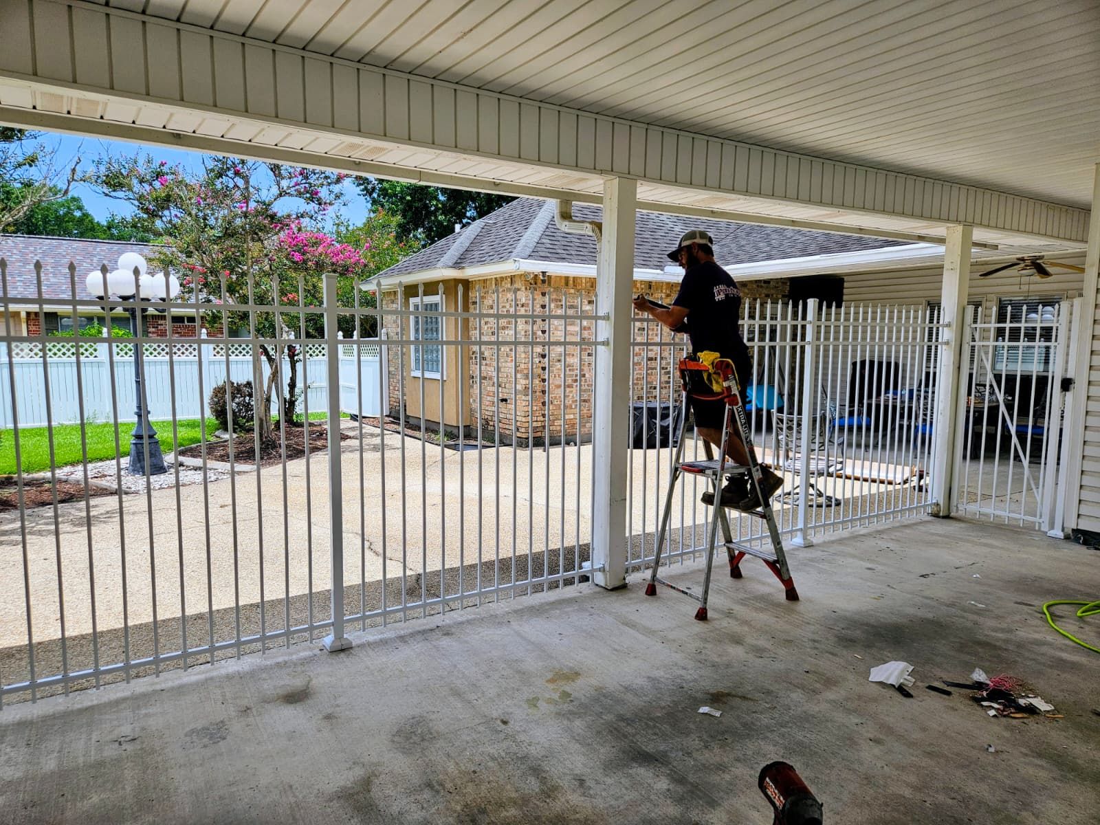 Person on a ladder painting a white fence in a covered patio area