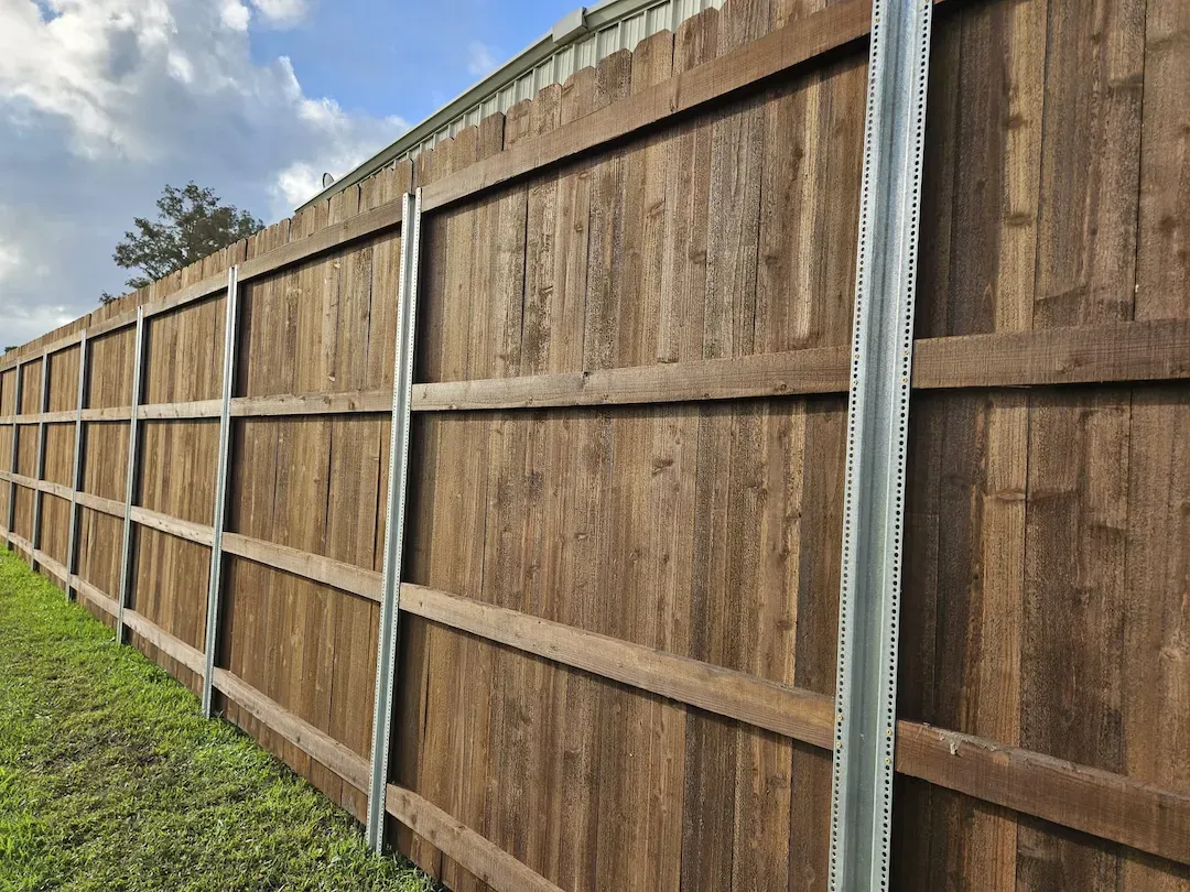 Long wooden privacy fence along a grassy yard under a cloudy sky