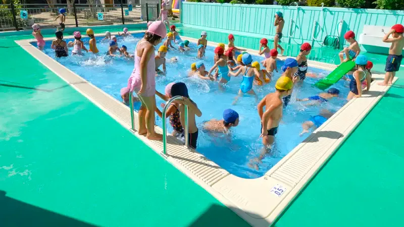 Children playing in a turquoise outdoor pool with a slide and splashing water