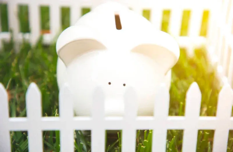 White pig figurine behind a white picket fence in a grassy yard