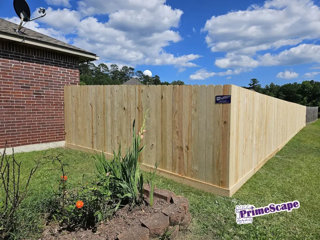 Wooden privacy fence enclosing a yard beside a brick house under a blue sky