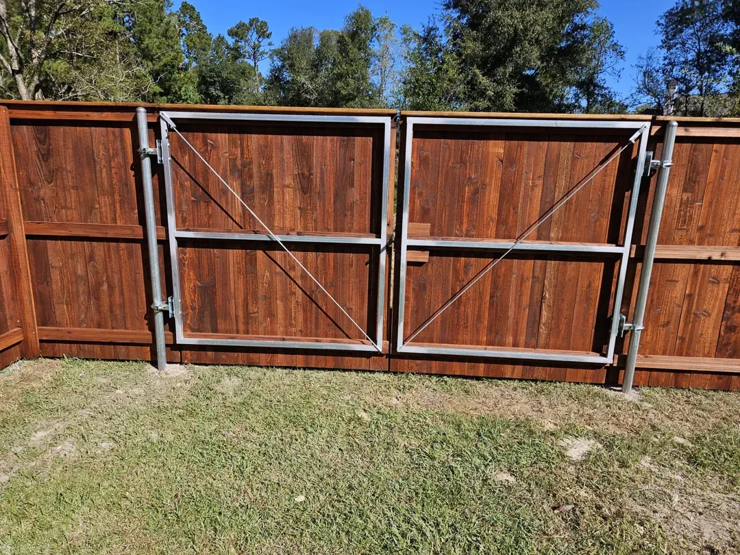Wooden backyard fence with a double gate and grass in front, under a clear blue sky