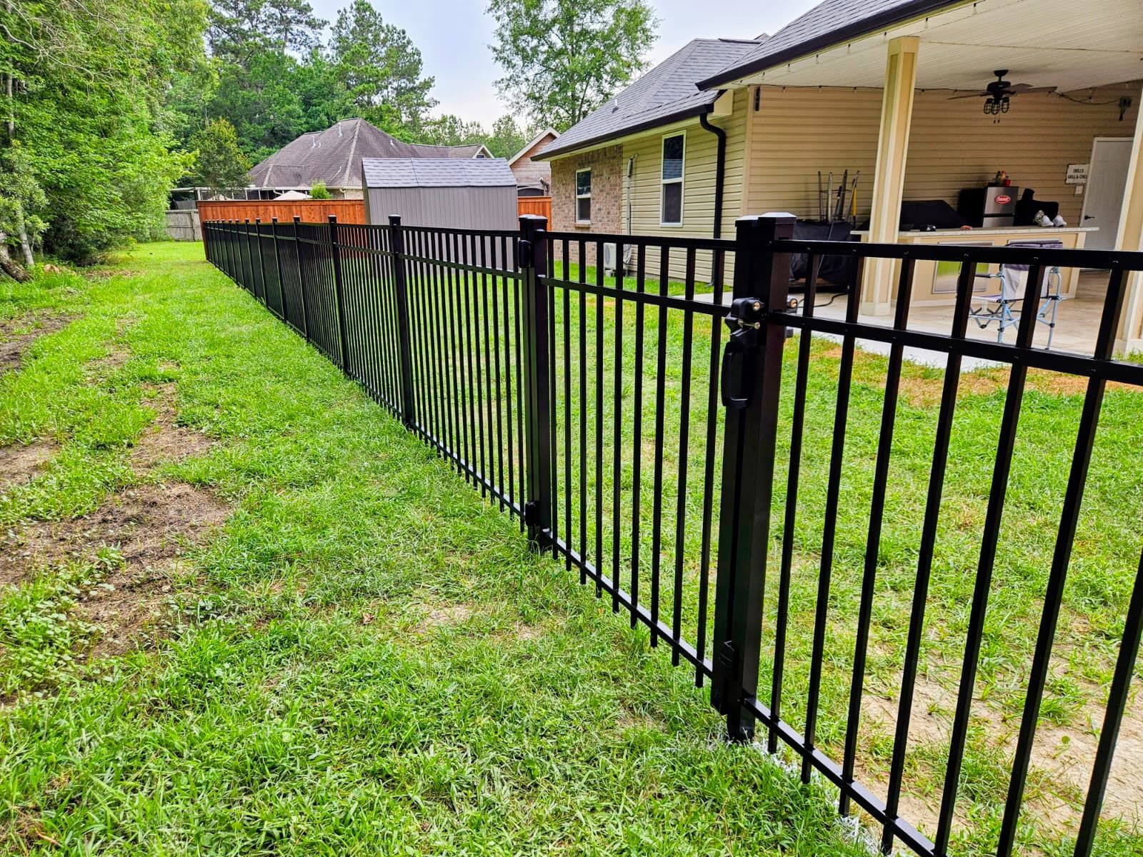 Black metal fence beside a grassy yard next to a house and covered porch
