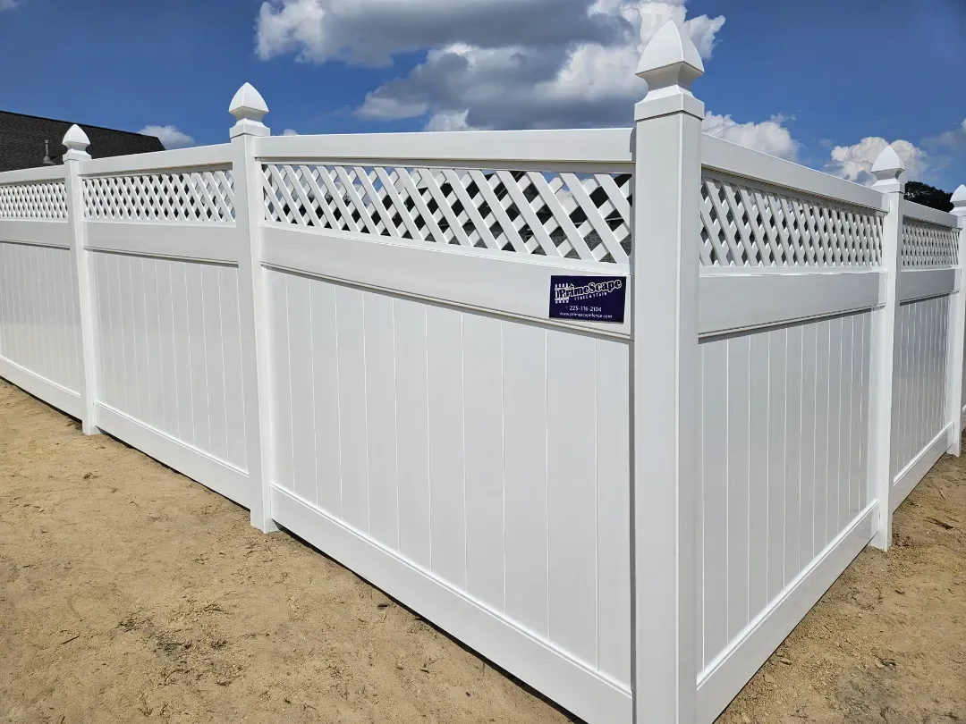 White vinyl privacy fence with lattice top in a sandy yard under a partly cloudy sky