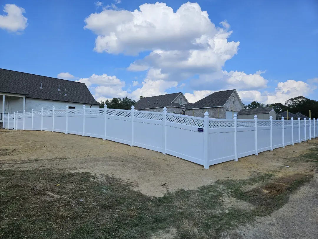White vinyl fence around a yard near houses under a partly cloudy blue sky