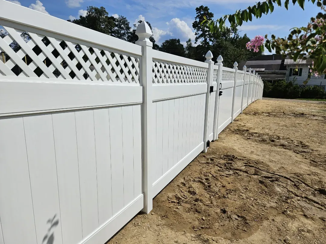 White vinyl fence lining a dirt lot under a blue sky