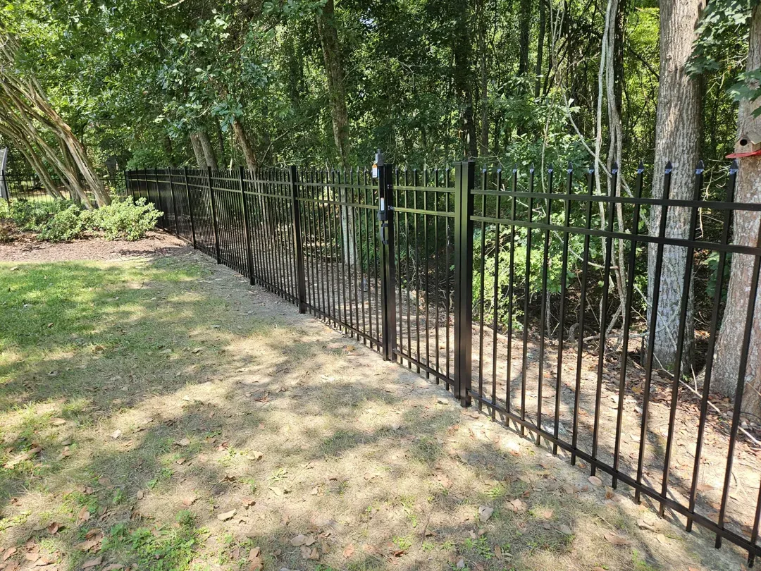 Black metal fence along a grassy yard beside a wooded area