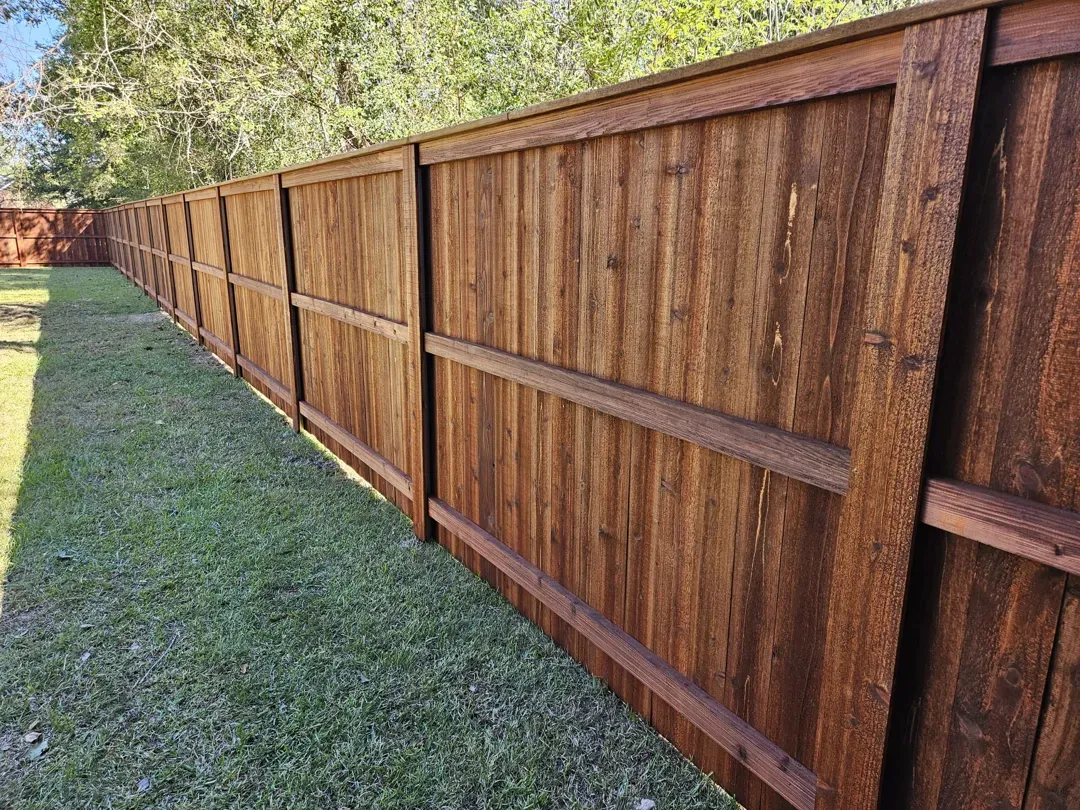 Long wooden privacy fence beside a grassy yard, stretching into the distance.