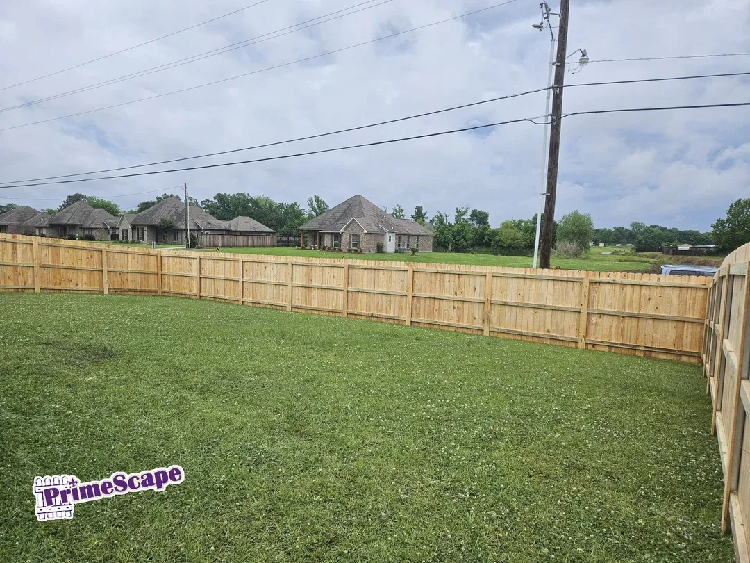 Grassy fenced backyard with a wooden privacy fence and cloudy sky overhead