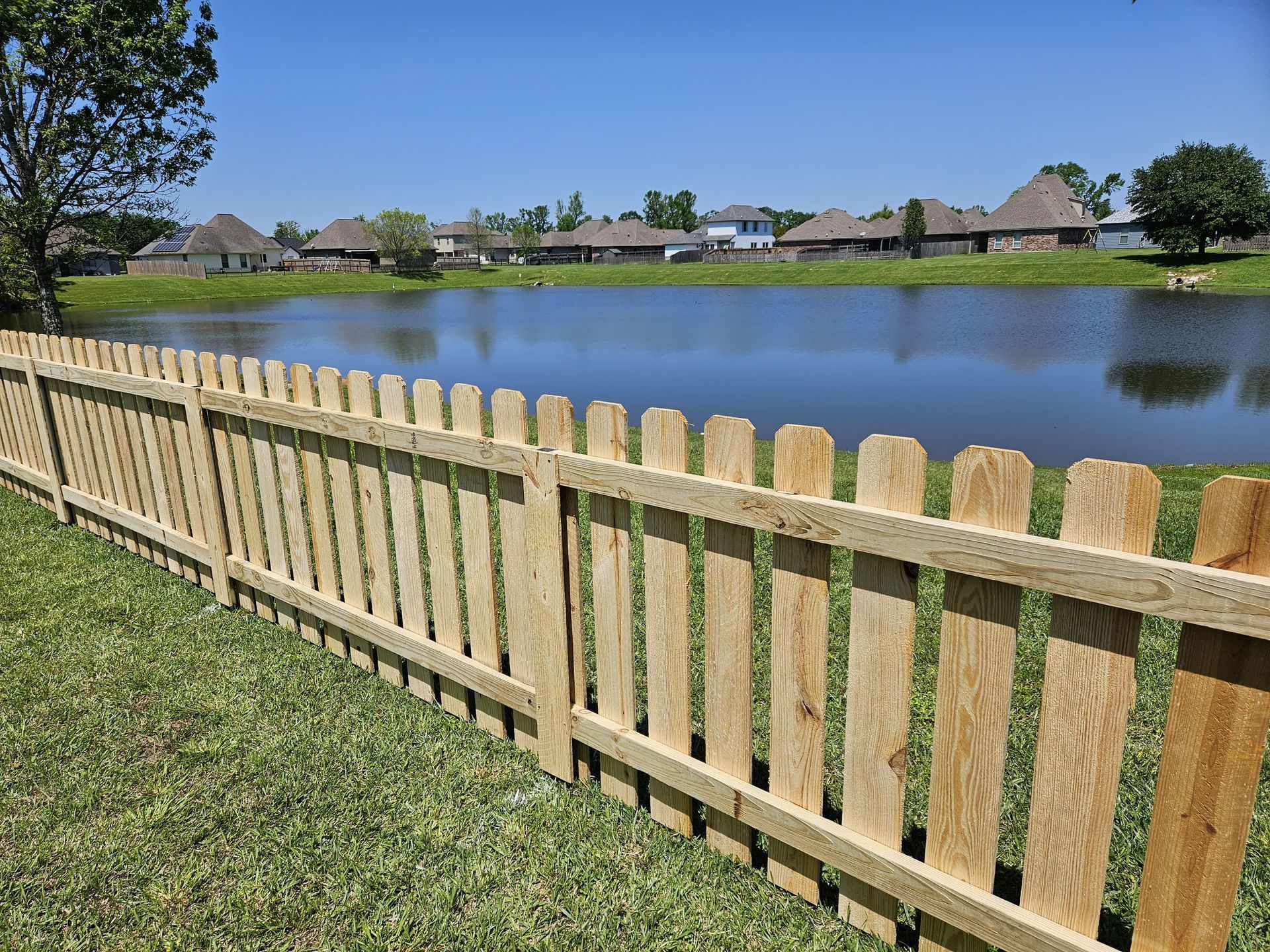 Wooden fence beside a calm lake in a suburban neighborhood under a clear blue sky