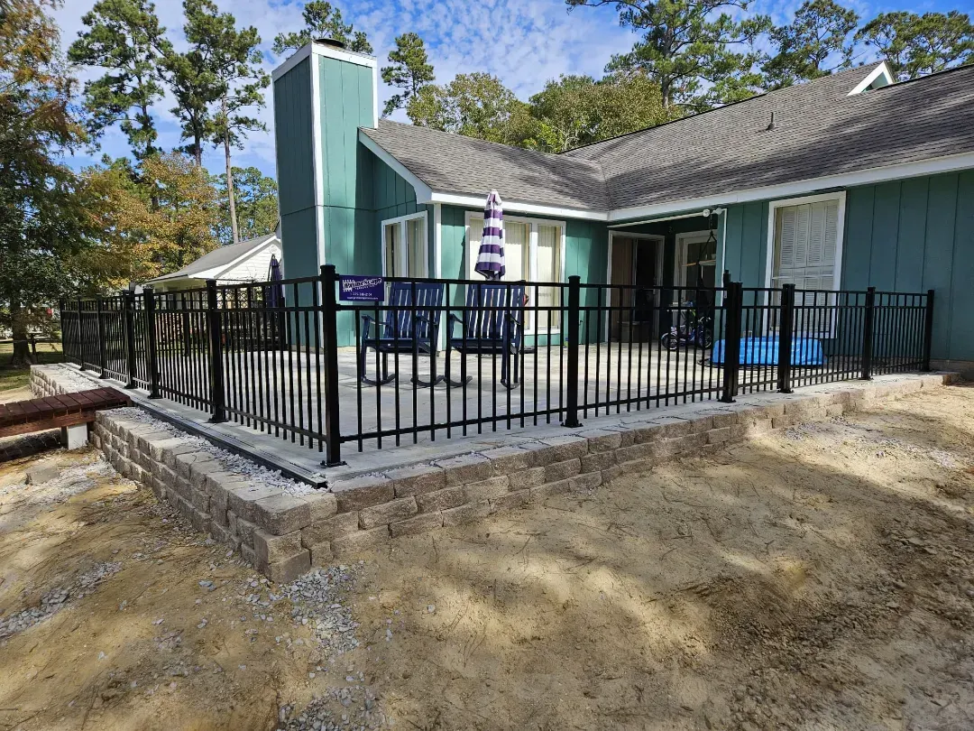 Accessible house porch with black railing, teal chimney, and chairs on a small concrete patio