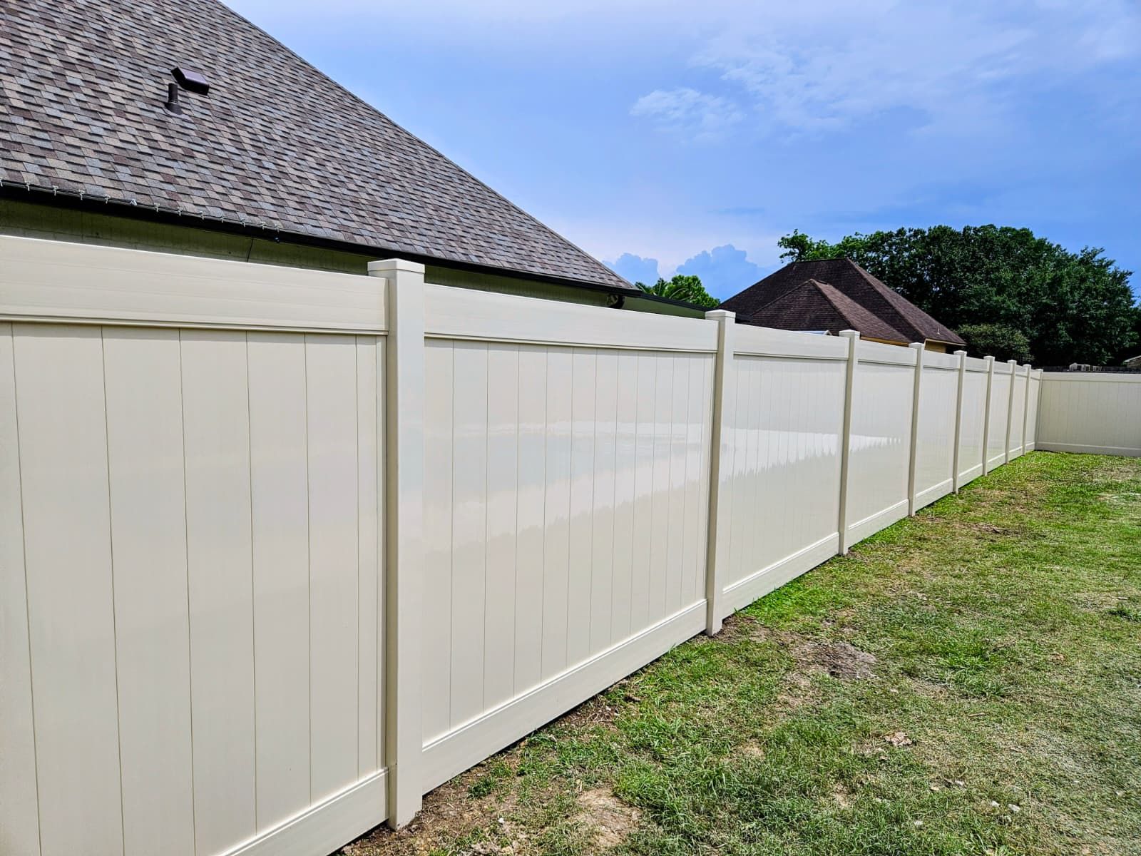 White vinyl fence along a grassy yard beside houses under a clear sky