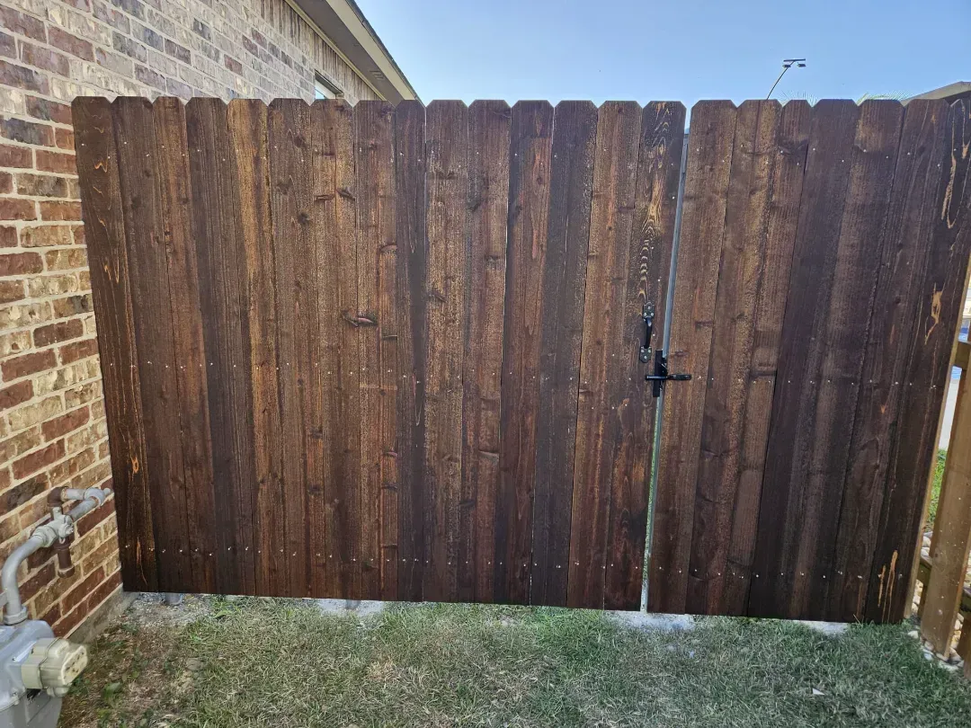 Rusty wooden backyard gate between a brick wall and fence.