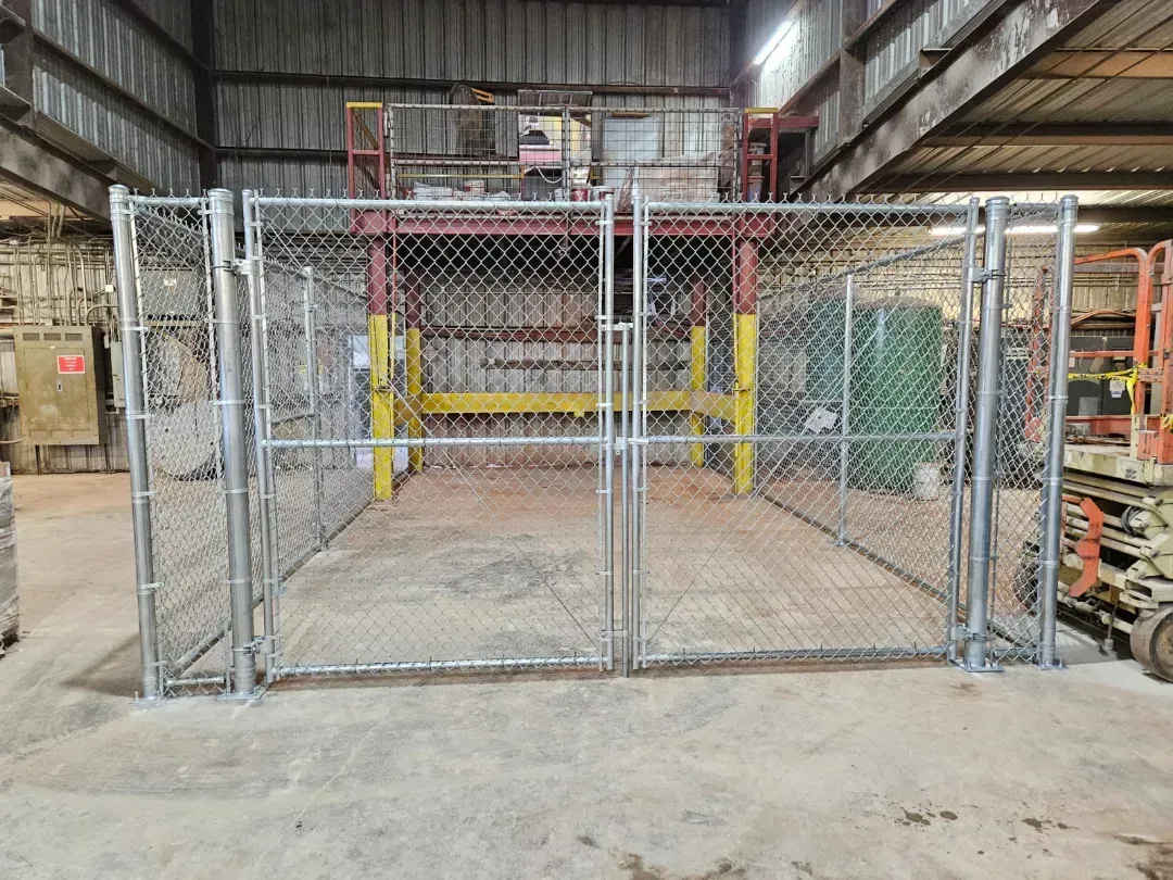 Chain-link gate enclosing a warehouse work area with yellow posts and industrial shelving.