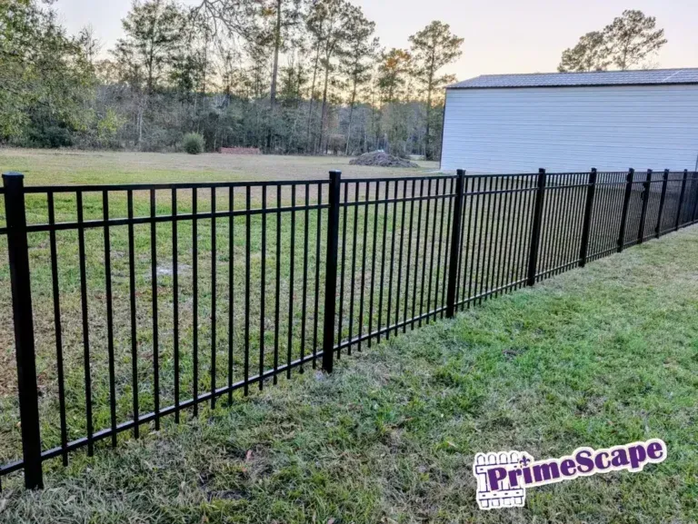 Black metal fence along grassy yard beside a house with trees in the background.