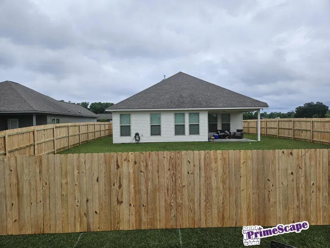 Backyard with tall wooden privacy fence around a white house under a cloudy sky