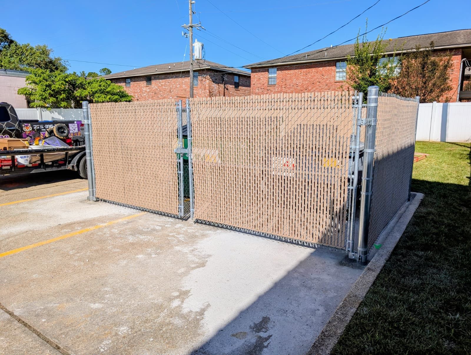 Closed beige wooden gate blocking a driveway beside a brick house on a sunny day